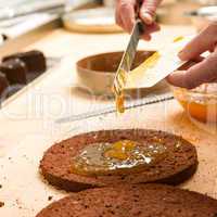 Cook making layer chocolate cake with marmalade