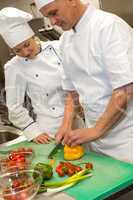 Apprentice learning cutting vegetables from chef