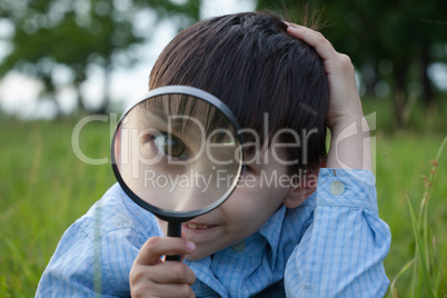 Boy with magnifying glass lying on the grass