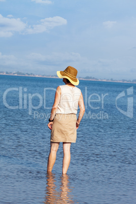 Woman with hat standing in the sea and looks into the distance