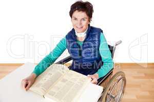Woman with book sitting in a wheelchair at the table