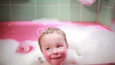 Two year old boy taking a bath with foam. Slow motion.