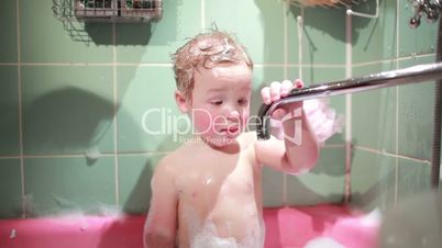 Two year old boy plays in the bath. Slow motion.