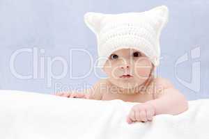 Beautiful baby in white hat lies on bed