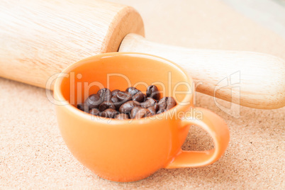 Cup of roast coffee bean and roller on cork background