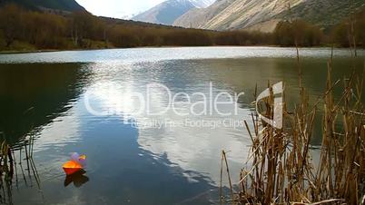 Orange paper boat floating in mountain lake