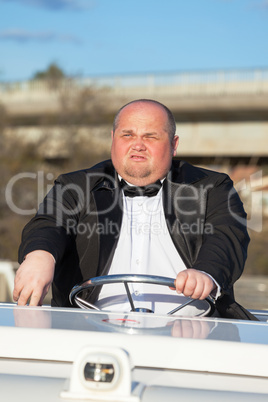 Overweight man in a tuxedo at the helm of a pleasure boat