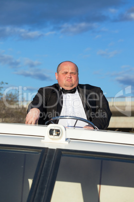 Overweight man in a tuxedo at the helm of a pleasure boat