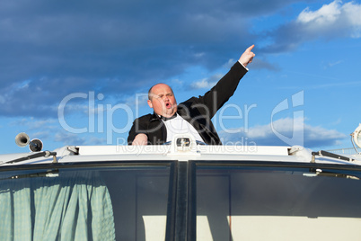 Overweight man in a tuxedo at the helm of a pleasure boat