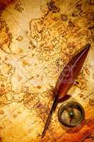 Vintage compass and goose quill pen lying on an old map.