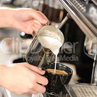 Waitress hands pouring milk making cappuccino
