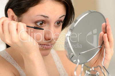 Attractive woman using mascara and handheld mirror