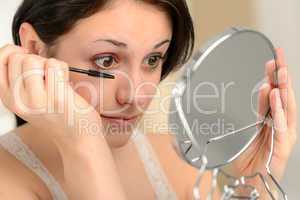 Attractive woman using mascara and handheld mirror