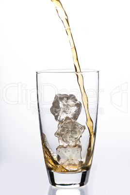 Liquid pouring into glass with ice cubes