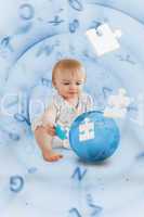 Baby holding a blue jigsaw piece sitting next to a globe