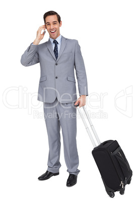 Smiling businessman with his luggage while phoning