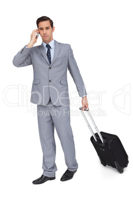 Serious businessman on the phone while holding his suitcase