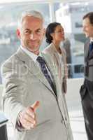 Businessman giving a handshake with colleagues behind