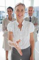 Smiling businesswoman giving a handshake with colleagues behind