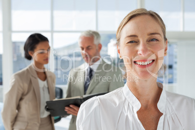 Cheerful businesswoman standing with colleagues working behind