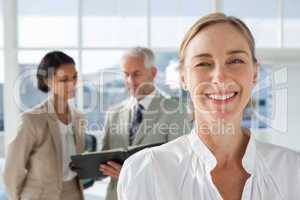 Cheerful businesswoman standing with colleagues working behind