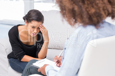 Woman crying on sofa while therapist is taking notes