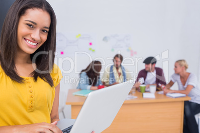 Woman using laptop with creative team working behind her