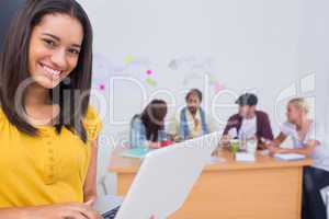 Woman using laptop with creative team working behind her