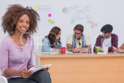 Happy editor using tablet as team works behind her