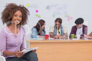 Happy editor using tablet as team works behind her