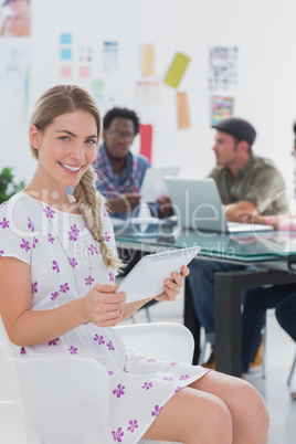 Editor holding tablet and smiling at camera as her team works be