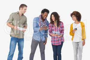 Four stylish friends looking at tablet and holding phones