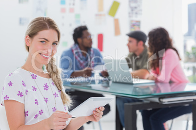 Smiling woman using tablet with creative team working behind