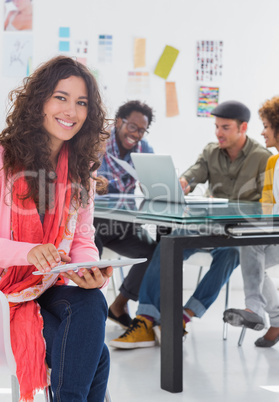 Smiling woman  using tablet with creative team working behind