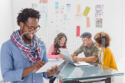 Smiling man using tablet with creative team working behind