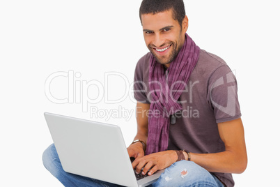 Smiling man sitting on floor using laptop looking at camera