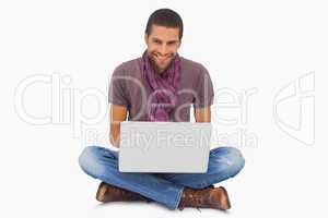 Stylish man sitting on floor using laptop and smiling at camera