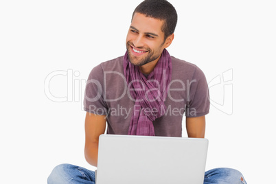 Fashionable man sitting on floor using laptop and looking away