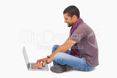 Man wearing scarf sitting on floor using laptop