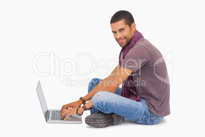 Fashionable man sitting on floor using laptop smiling at camera