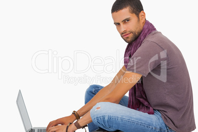 Serious man wearing scarf sitting on floor using laptop