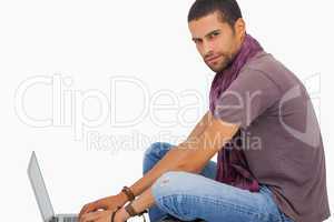 Serious man wearing scarf sitting on floor using laptop