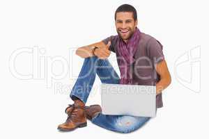 Happy man sitting on floor using laptop giving thumbs up