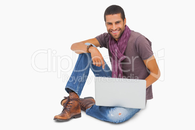 Happy man sitting on floor using laptop looking at camera