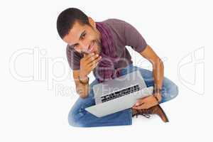 Thoughtful man sitting on floor using laptop and smiling at came