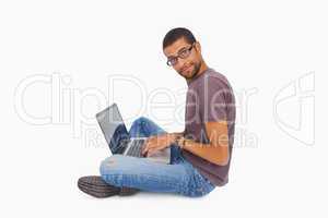 Man wearing glasses sitting on floor using laptop and looking at