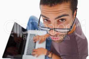 Man wearing glasses sitting on floor using laptop and looking up