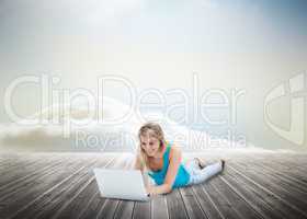 Cute blonde woman laying and using laptop over wooden boards