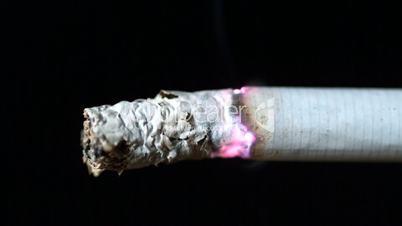 Cigarette burning on black background close up