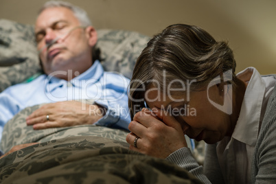 Uneasy senior woman praying for sick man